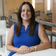 Smiling woman sitting indoors, wearing blue dress.