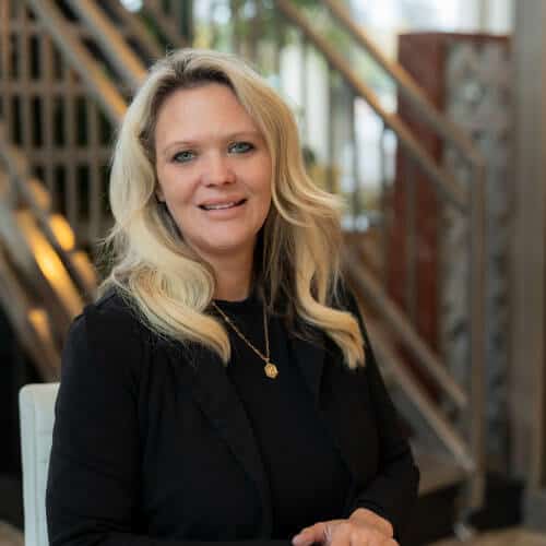 Smiling woman in black suit indoors, modern setting.